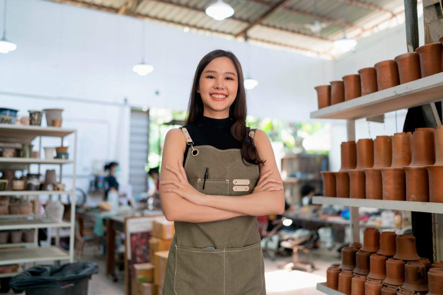 Young woman in pottery studio smiling confidently with arms crossed.